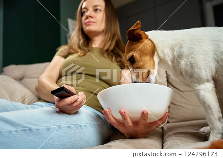 Woman watching TV while dog steals food from bowl 124296173