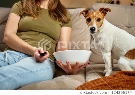 Woman relaxing on sofa with pet dog and snack bowl 124296174