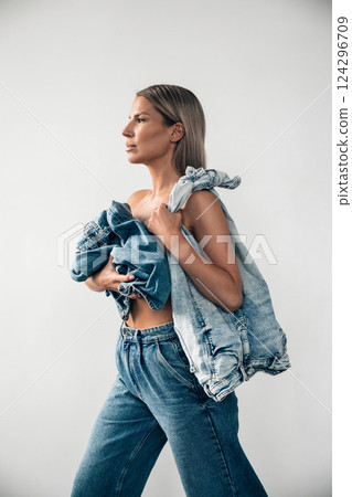 Fashionable woman poses with denim apparel in stylish outfit against a minimalist background Fashionable woman poses with denim apparel in stylish outfit against a minimalist background 124296709