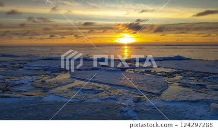 Breathtaking winter sunset over a frozen sea, with colorful orange and yellow hues reflecting on the icy surface. Breathtaking winter sunset over a frozen sea, with colorful orange and yellow hues reflecting on the icy surface. 124297288
