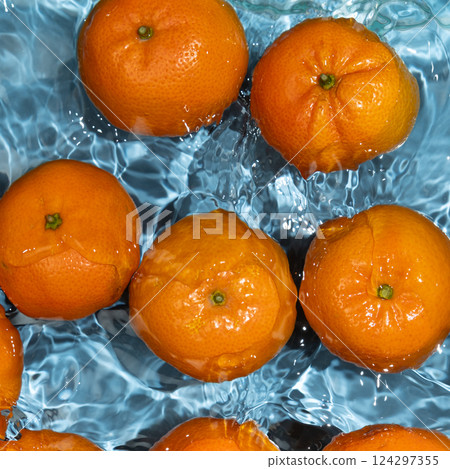 Whole unpeeled fresh fruit tangerines in water, splash of water, refreshing juicy background top view. Whole unpeeled fresh fruit tangerines in water, splash of water, refreshing juicy background top view. 124297355