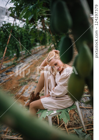 Young woman relaxing amidst green plants in a greenhouse setting during daylight hours Young woman relaxing amidst green plants in a greenhouse setting during daylight hours 124297379