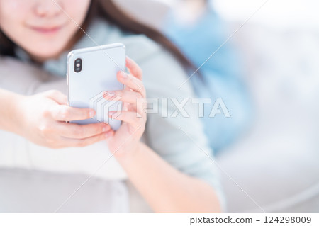 A young woman lying down and relaxing while looking at her smartphone, no face A young woman lying down and relaxing while looking at her smartphone, no face 124298009