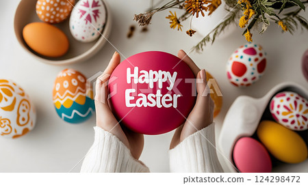 Happy Easter, hands holding a festive pink egg with white lettering, surrounded by colorful eggs Happy Easter, hands holding a festive pink egg with white lettering, surrounded by colorful eggs 124298472