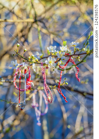 Traditional Symbol of spring in Balkans hanging on tree branch. Red Martenitsa bracelets tied to blossoming tree with flowers in early spring. Symbol of renewal, good fortune in Bulgarian folklore 124298576