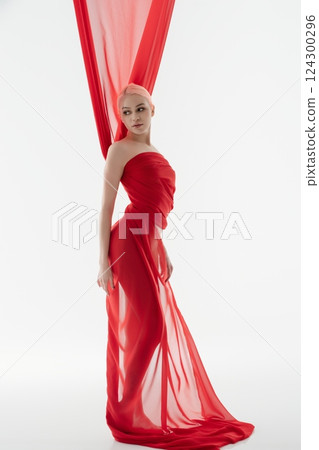 Elegant woman in flowing red fabric poses gracefully in soft light Elegant woman in flowing red fabric poses gracefully in soft light 124300296