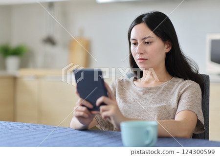Asian woman reading ebook sitting in a kitchen 124300599