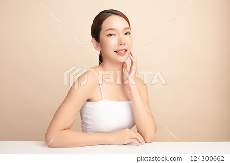 A beautiful young Asian woman with clean, fresh skin against a beige background. Skincare, facial treatment, cosmetology, beauty, and spa. An elegant portrait of an Asian woman. 124300662
