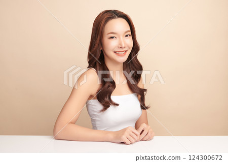 A beautiful young Asian woman with clean, fresh skin against a beige background. Skincare, facial treatment, cosmetology, beauty, and spa. An elegant portrait of an Asian woman. 124300672