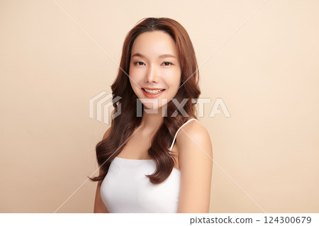 A beautiful young Asian woman with clean, fresh skin against a beige background. Skincare, facial treatment, cosmetology, beauty, and spa. An elegant portrait of an Asian woman. 124300679