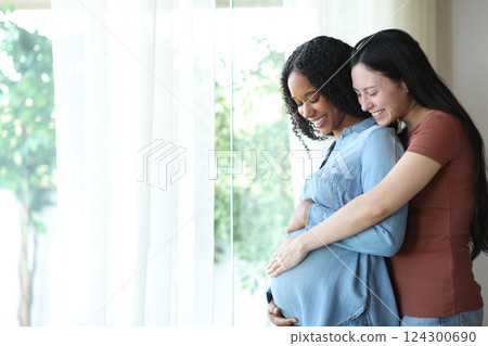 Proud interracial lesbian couple enjoying pregnancy at home Proud interracial lesbian couple enjoying pregnancy at home 124300690