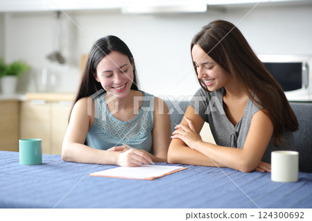 Two happy interracial roommates signing paper contract Two happy interracial roommates signing paper contract 124300692
