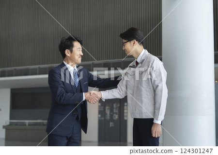 A businessman in a suit and a man in work clothes shaking hands 124301247