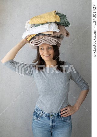 washing clothes, a woman holds a stack of clothes on her head after dry cleaning. housework. washing clothes, a woman holds a stack of clothes on her head after dry cleaning. housework. 124301427