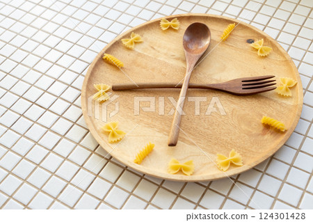 time to eat pasta. wooden plate with fork and spoon in form of clock hands. pasta on plate. time to eat pasta. wooden plate with fork and spoon in form of clock hands. pasta on plate. 124301428
