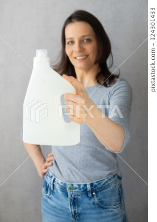 mockup, happy woman holds in her hands a washing gel or conditioner for washing clothes. mockup, happy woman holds in her hands a washing gel or conditioner for washing clothes. 124301433