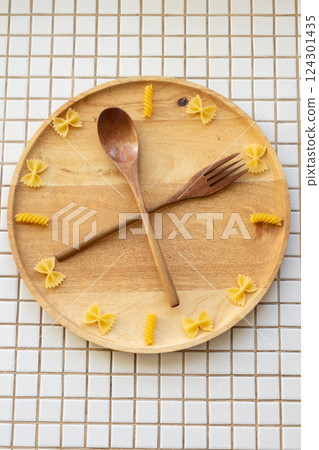 time to eat pasta. wooden plate with fork and spoon in form of clock hands. pasta on plate. time to eat pasta. wooden plate with fork and spoon in form of clock hands. pasta on plate. 124301435
