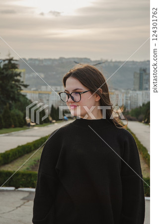 Pensive young woman in black sweater enjoying a peaceful park stroll at sunset. Glasses for vision 124301762