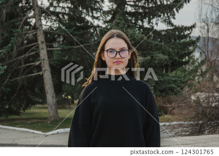 Portrait of a young woman in glasses outdoors with pine trees in the background. Glasses for vision Portrait of a young woman in glasses outdoors with pine trees in the background. Glasses for vision 124301765