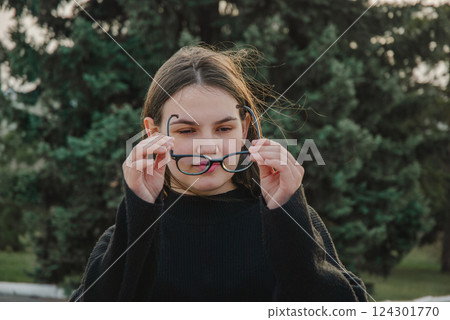 Young woman adjusting glasses in park setting. Glasses for vision Young woman adjusting glasses in park setting. Glasses for vision 124301770