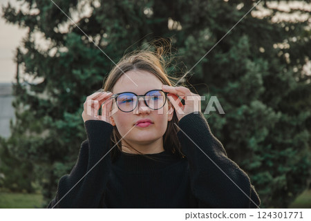 Young woman outdoors adjusting glasses in a park setting. Glasses for vision Young woman outdoors adjusting glasses in a park setting. Glasses for vision 124301771