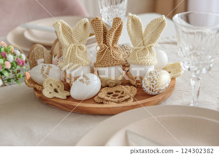 Festive Easter table setting with several Easter bunny made from egg and knitted ears on wooden plate. Easter celebration concept Festive Easter table setting with several Easter bunny made from egg and knitted ears on wooden plate. Easter celebration concept 124302382