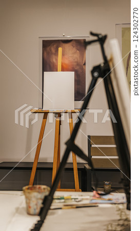 Creative space, blank canvas on easel with paint supplies. An art studio with blank canvas on an easel, paintbrushes, palettes. Light fills the space, concept of inspiring, creativity and expression 124302770