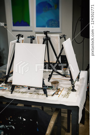 Easels in a Studio, art school for adults. Wooden Easels With Canvas, Art supplies on table near easel with canvas indoors. Painting Lessons in artist studio Easels in a Studio, art school for adults. Wooden Easels With Canvas, Art supplies on table near easel with canvas indoors. Painting Lessons in artist studio 124302771