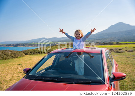 Little girl joyfully sticks out of car sunroof with raised hands against the backdrop of mountains in Northern Cyprus. The image symbolizes freedom, adventure, and the excitement of travel with child 124302889