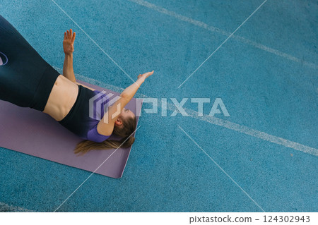 A woman practices yoga on a purple mat in a serene gym during a peaceful morning session A woman practices yoga on a purple mat in a serene gym during a peaceful morning session 124302943