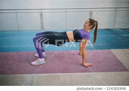 Fit woman performing a bridge exercise on a yoga mat by the waterfront in the early morning Fit woman performing a bridge exercise on a yoga mat by the waterfront in the early morning 124302946