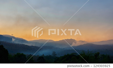 Wildfire disaster is burning forests on the mountains. Emergency services helicopter drops water to extinguish the forest fires that burned the forest on the mountains. 124303925
