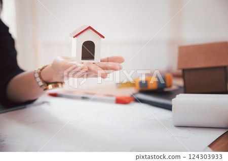 Woman holding house model while sitting in front of her working place. Woman holding house model while sitting in front of her working place. 124303933