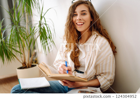 Young woman reading book, writing notes, doing homework at home. Concept of rest, relaxation. Young woman reading book, writing notes, doing homework at home. Concept of rest, relaxation. 124304952