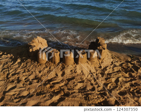 Detailed sandcastle standing firm against soft adriatic waves, nestled on golden sands of bibione shoreline Detailed sandcastle standing firm against soft adriatic waves, nestled on golden sands of bibione shoreline 124307350