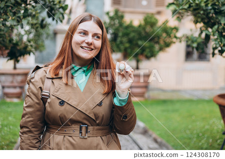 Happy 30s woman holding Sicilian cannolo tube pastry filled with cream outdoors. Travel, Italy, food and holidays concept. Young woman eating traditional delicious cake cannoli, Traveling Europe 124308170