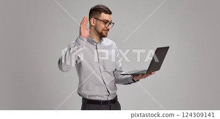 Smiling employee raising hand in front of laptop during video call and waving to colleagues Smiling employee raising hand in front of laptop during video call and waving to colleagues 124309141