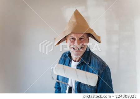 Senior man painting walls with roller in new home, looking at camera. 124309325