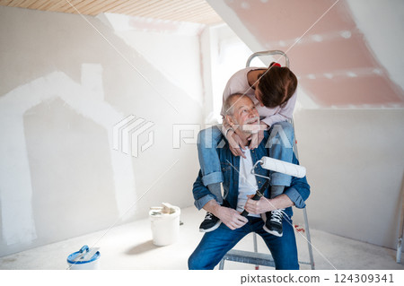 Senior husband and wife standing on a ladder repainting the walls. 124309341