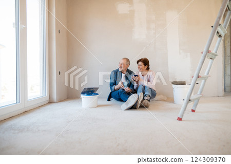 Senior couple resting while painting walls in new home, having coffee. 124309370