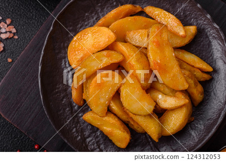 Baked potato wedges with cheese and herbs on a dark background 124312053