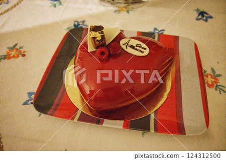 A beautiful red heart-shaped French birthday cake with a raspberry topping, elegantly placed on a white tablecloth A beautiful red heart-shaped French birthday cake with a raspberry topping, elegantly placed on a white tablecloth 124312500