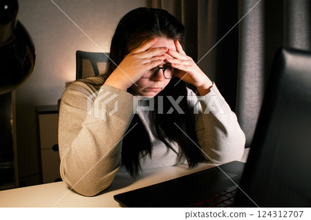 Hard working woman works on computer in her home office and tries to solve work problems. Feeling despair and burnt out from job issues. Hard working woman works on computer in her home office and tries to solve work problems. Feeling despair and burnt out from job issues. 124312707