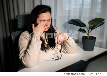 Tired woman working at home with laptop holding eyeglasses rubbing eyes and feeling fatigue. Stress and frustration concept. Tired eyes Tired woman working at home with laptop holding eyeglasses rubbing eyes and feeling fatigue. Stress and frustration concept. Tired eyes 124312713