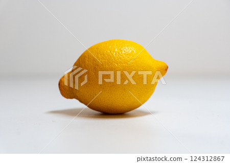 There is a bright yellow lemon that is resting on a white surface There is a bright yellow lemon that is resting on a white surface 124312867