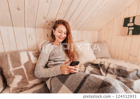 Woman Texting with Smart Phone in Bed in Log Cabin Woman Texting with Smart Phone in Bed in Log Cabin 124312931
