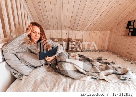 Woman Reading Book in Bed at Cozy Log Cabin Woman Reading Book in Bed at Cozy Log Cabin 124312933