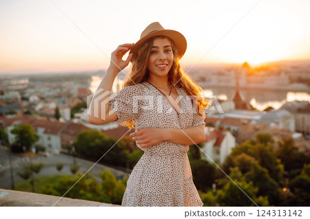 Smiling female tourist in hat admires landscape of city at dawn. Euro-trip. Active lifestyle concept Smiling female tourist in hat admires landscape of city at dawn. Euro-trip. Active lifestyle concept 124313142