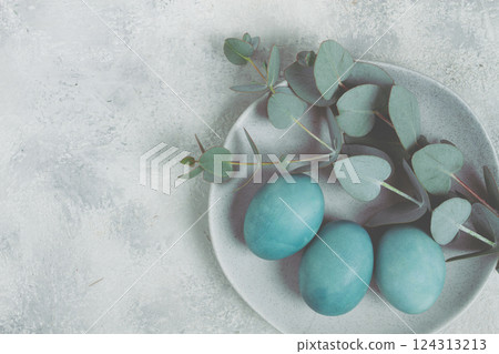 Easter colored eggs, in turquoise tones, on a gray plate, with a branch of eucalyptus, Easter card, top view, no people 124313213