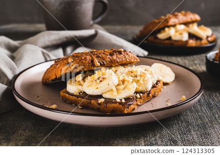 Sweet sandwich with chocolate butter, banana and nuts on a plate on the table 124313305